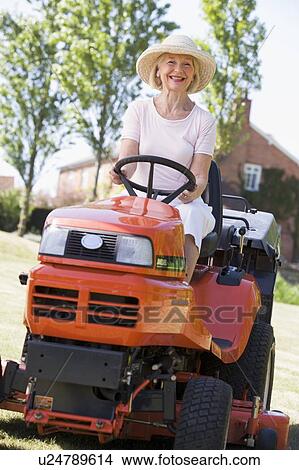 Picture - Woman outdoors driving lawnmower smiling. Fotosearch