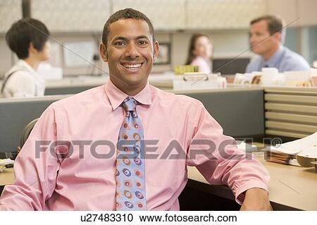 Stock Image - Businessman in cubicle smiling. Fotosearch