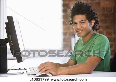 Stock Photo - Businessman in office using computer and smiling. Fotosearch