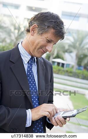 Stock Photo - Businessman outdoors using personal digital assistant smiling. Fotosearch