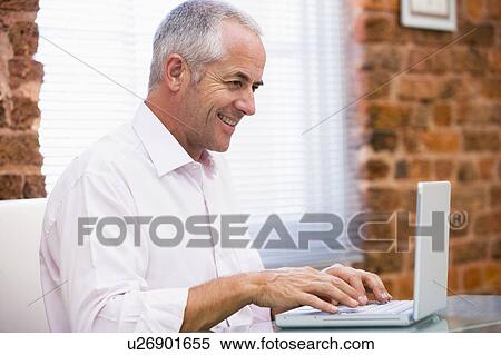 Stock Photography - Businessman sitting in office typing on laptop smiling. Fotosearch