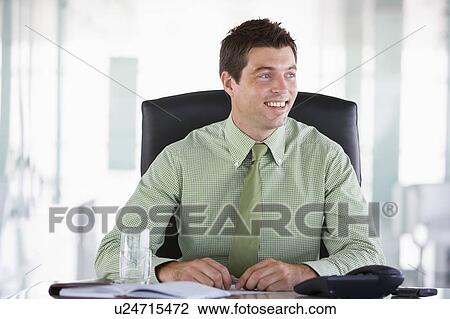 Stock Image - Businessman sitting in office with personal organizer smiling. Fotosearch
