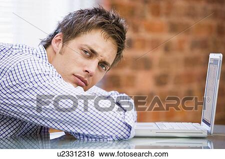 Stock Photo - Businessman sitting in office with laptop looking unhappy. Fotosearch