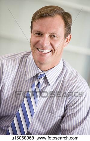 Businessman sitting indoors smiling View Large Photo Image Stock Photo - Businessman sitting indoors smiling. Fotosearch