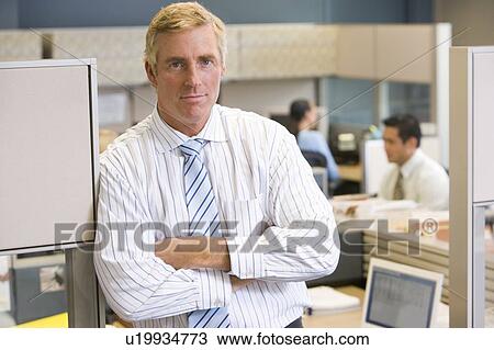 Stock Image - Businessman standing in cubicle. Fotosearch