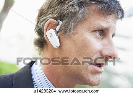Picture - Businessman wearing earpiece outdoors. Fotosearch