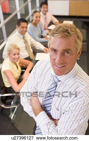 Stock Photo - Businessman with four businesspeople at boardroom table in background. Fotosearch