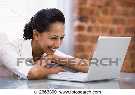 Stock Image - Businesswoman in office with laptop laughing. Fotosearch