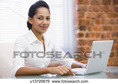 Stock Photo - Businesswoman in office with laptop smiling. Fotosearch