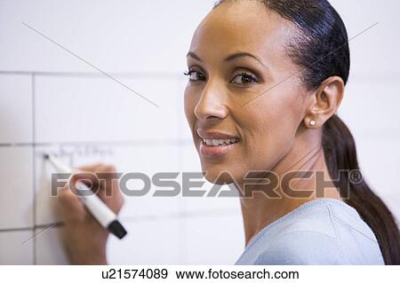 Businesswoman indoors writing on erasable board smiling View Large Photo Image Stock Photo - Businesswoman indoors writing on erasable board smiling. Fotosearch