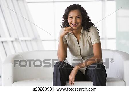 Stock Image - Businesswoman sitting indoors smiling (high key/selective focus). Fotosearch