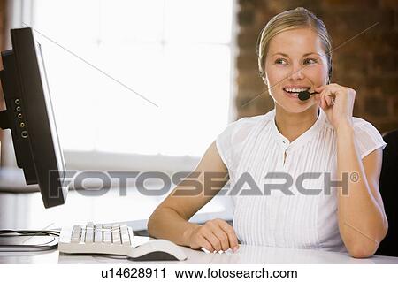 Stock Image - Businesswoman wearing headset in office smiling. Fotosearch