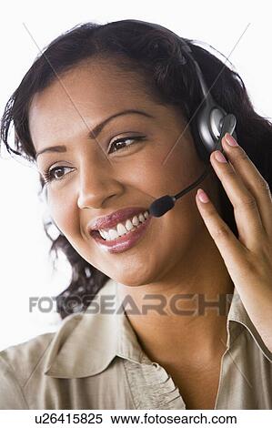Stock Photography - Businesswoman wearing headset in office smiling (high key/selective focus). Fotosearch