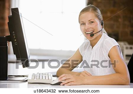 Stock Image - Businesswoman wearing headset sitting in office smiling. Fotosearch