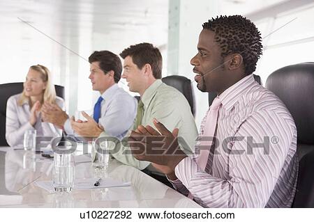 Stock Image - Four businesspeople in a boardroom applauding. Fotosearch