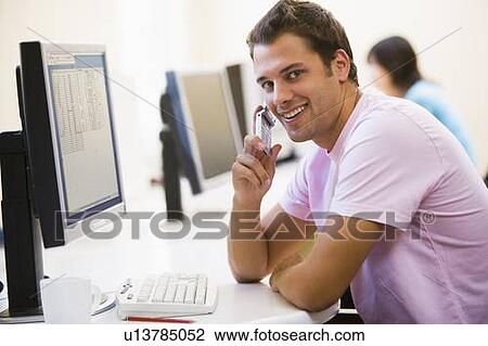 Man sitting in computer room using cellular phone and smiling View Large Photo Image Stock Image - Man sitting in computer room using cellular phone and smiling. Fotosearch