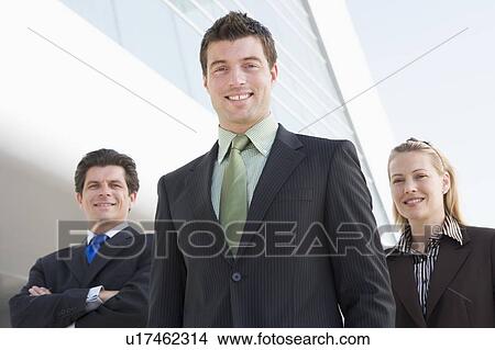Picture - Three businesspeople standing outdoors by building smiling. Fotosearch