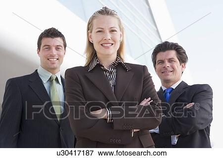 Stock Photo - Three businesspeople standing outdoors by building smiling. Fotosearch