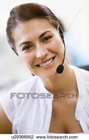 Stock Image - Woman wearing headset indoors smiling. Fotosearch