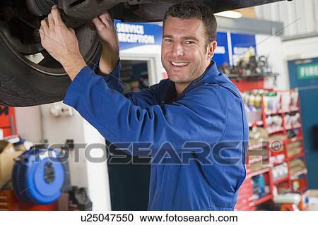 Stock Image - Mechanic working under car smiling. Fotosearch