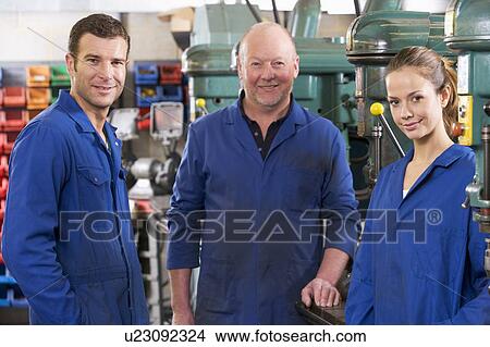 Picture - Three machinists in workspace by machine talking. Fotosearch