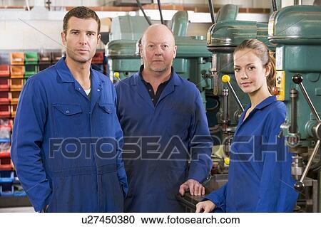 Stock Image - Three machinists in workspace by machine talking. Fotosearch