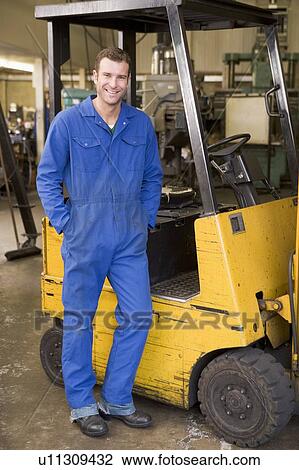 Warehouse worker standing by forklift View Large Photo Image Stock Image - Warehouse worker standing by forklift. Fotosearch
