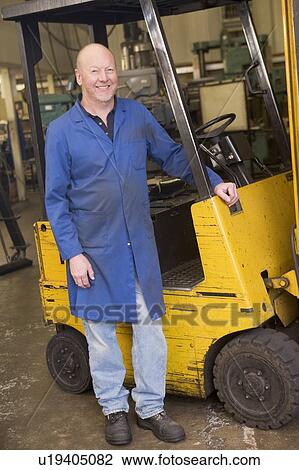 Stock Image - Warehouse worker standing by forklift. Fotosearch