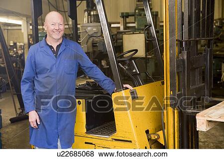 Warehouse worker standing by forklift View Large Photo Image Stock Photo - Warehouse worker standing by forklift. Fotosearch
