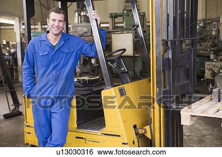 Warehouse worker standing by forklift View Large Photo Image Stock Photograph - Warehouse worker standing by forklift. Fotosearch