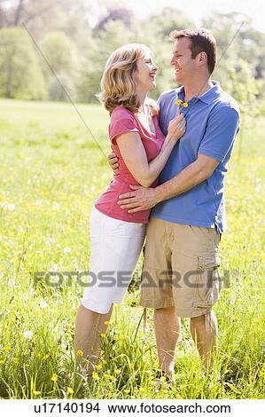Picture - Couple embracing outdoors holding flower smiling. Fotosearch