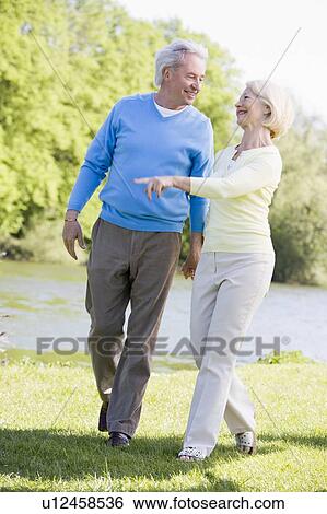 Stock Photograph - Couple walking outdoors at park by lake smiling. Fotosearch