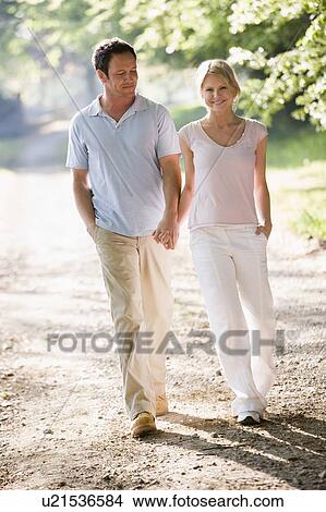 Couple walking outdoors holding hands and smiling View Large Photo Image Picture - Couple walking outdoors holding hands and smiling. Fotosearch