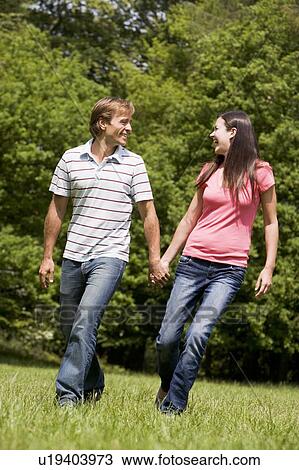 Stock Image - Couple walking outdoors holding hands smiling. Fotosearch