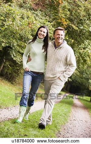 Stock Image - Couple walking outdoors on path in park smiling (selective focus). Fotosearch
