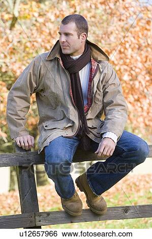 Stock Photograph - Man outdoors at park sitting on fence (selective focus). Fotosearch