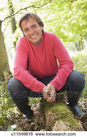 Stock Photograph - Man outdoors in woods sitting on log smiling. Fotosearch