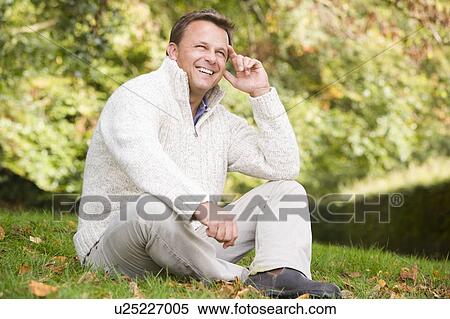 Stock Photography - Man sitting outdoors smiling (selective focus). Fotosearch