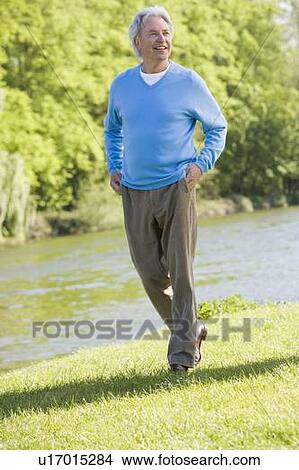 Picture - Man walking outdoors at park by lake smiling. Fotosearch