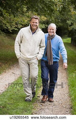 Two men walking on path outdoors smiling (selective focus) View Large Photo Image Stock Photography - Two men walking on path outdoors smiling (selective focus). Fotosearch