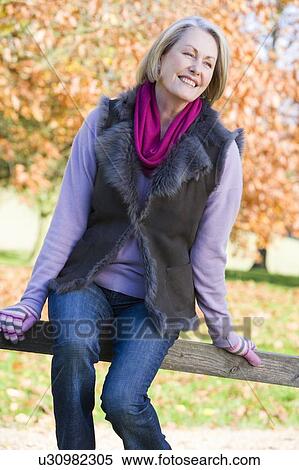 Woman outdoors at park sitting on fence smiling (selective focus) View Large Photo Image Stock Photography - Woman outdoors at park sitting on fence smiling (selective focus). Fotosearch