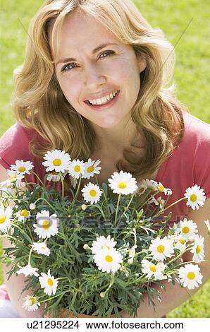 Woman outdoors holding flowers smiling View Large Photo Image Picture - Woman outdoors holding flowers smiling. Fotosearch