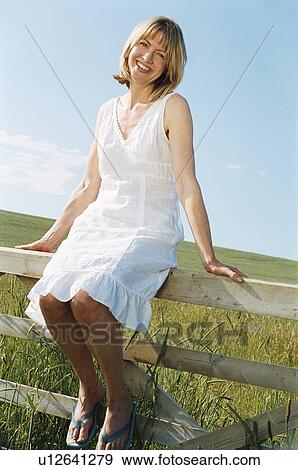 Woman sitting on fence outdoors smiling View Large Photo Image Stock Photo - Woman sitting on fence outdoors smiling. Fotosearch