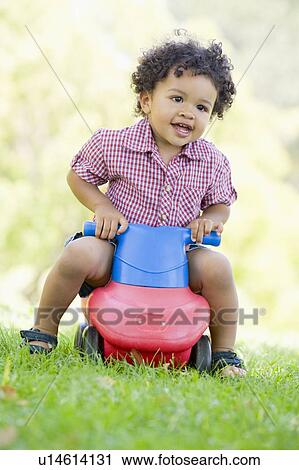 Stock Image - Young boy playing on toy with wheels outdoors. Fotosearch