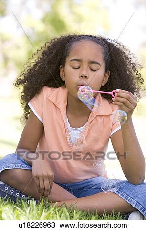 Stock Image - Young girl blowing bubbles outdoors. Fotosearch