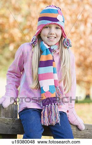 Stock Photo - Young girl outdoors at park sitting on fence smiling (selective focus). Fotosearch