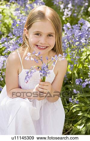 Stock Photo - Young girl outdoors holding flowers smiling. Fotosearch
