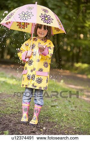 Stock Image - Young girl outdoors in rain with umbrella smiling. Fotosearch