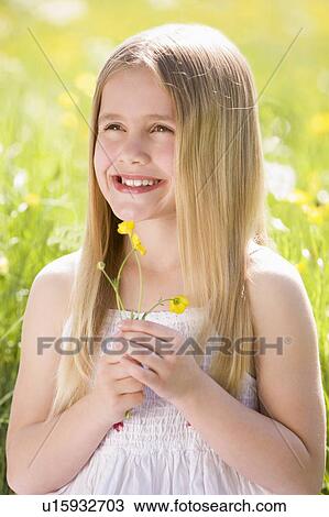 Young girl sitting outdoors holding flower smiling View Large Photo Image Stock Image - Young girl sitting outdoors holding flower smiling. Fotosearch