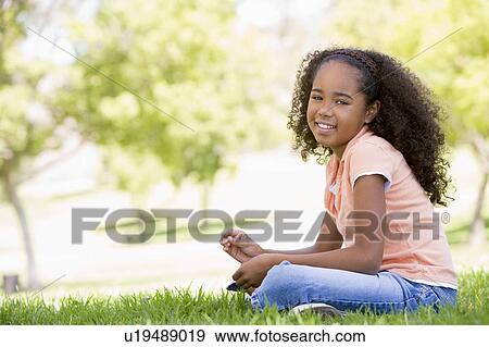 Young girl sitting outdoors smiling View Large Photo Image Stock Photo - Young girl sitting outdoors smiling. Fotosearch